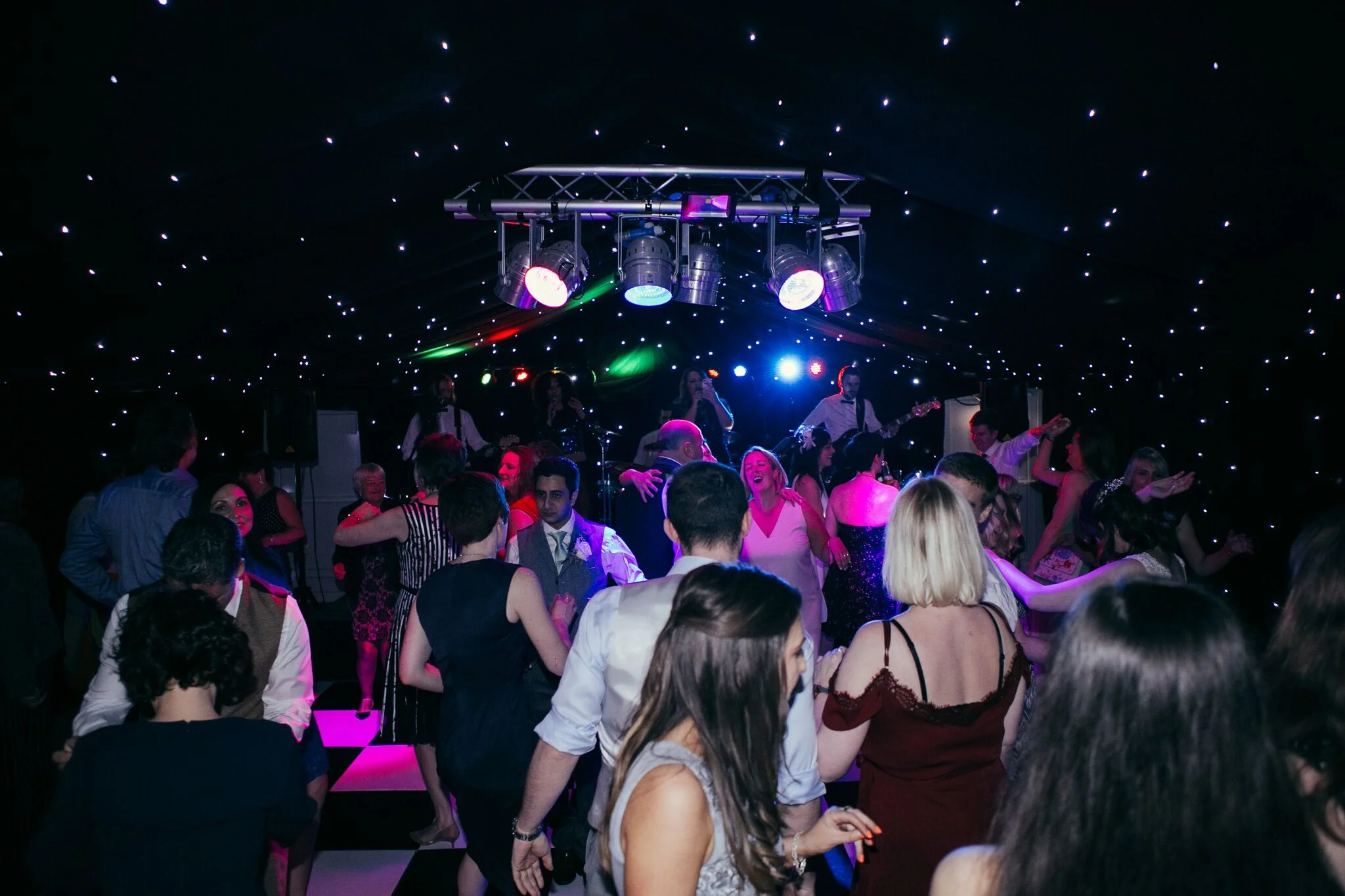 Wedding guests filling the chequered dance floor while the live band performs beneath a star-lit backdrop