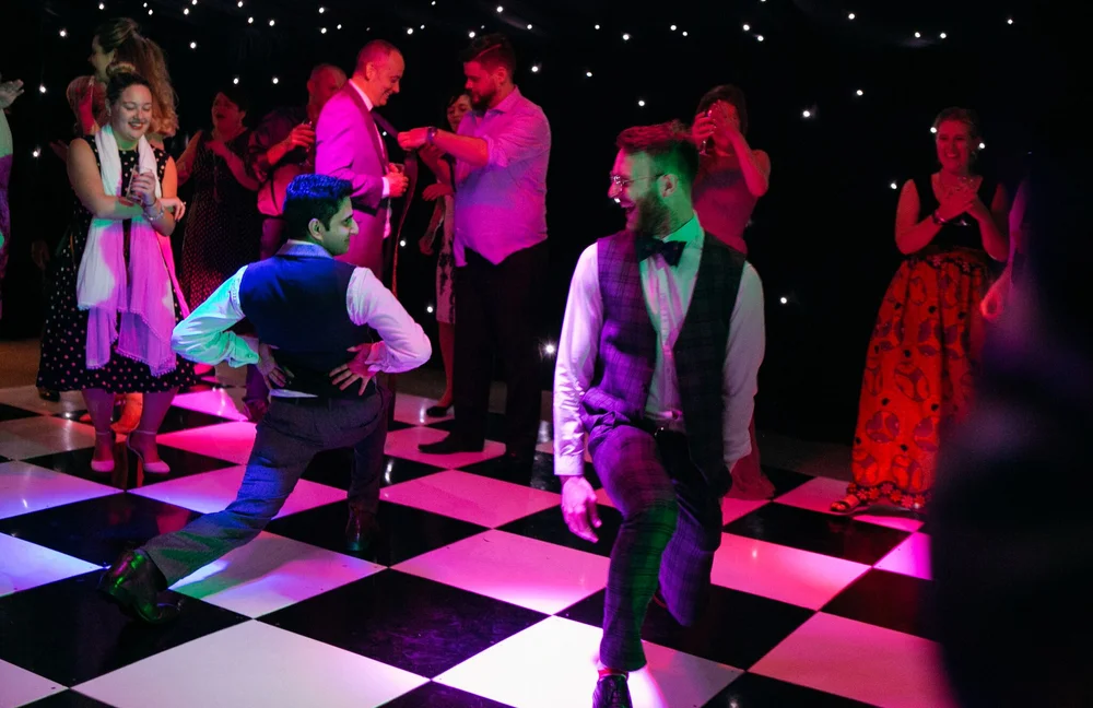 Two wedding guests showing their dance moves as friends cheer around the chequered floor