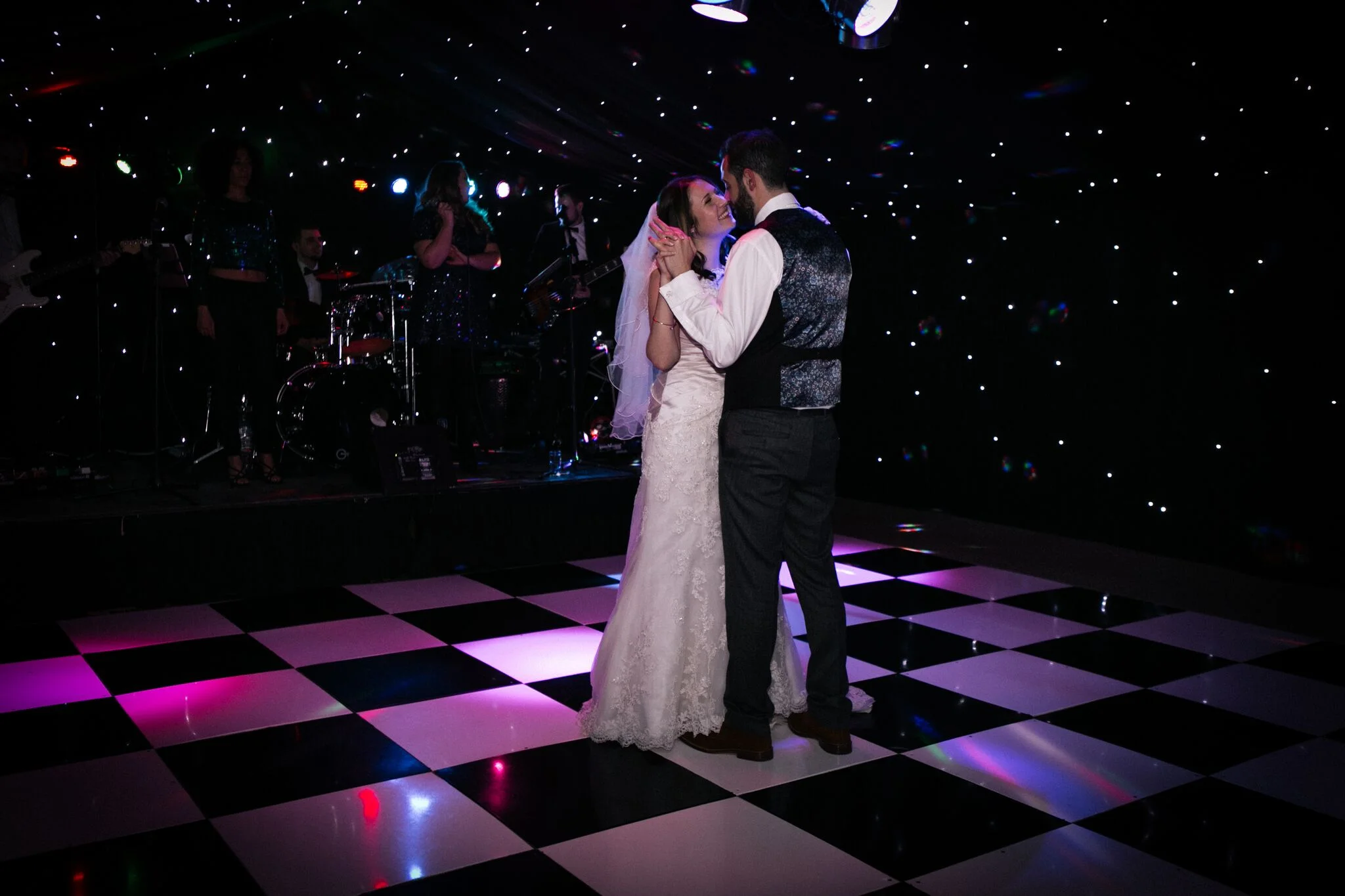 The bride and groom sharing their first dance on a chequered floor, with the five-piece band onstage behind them