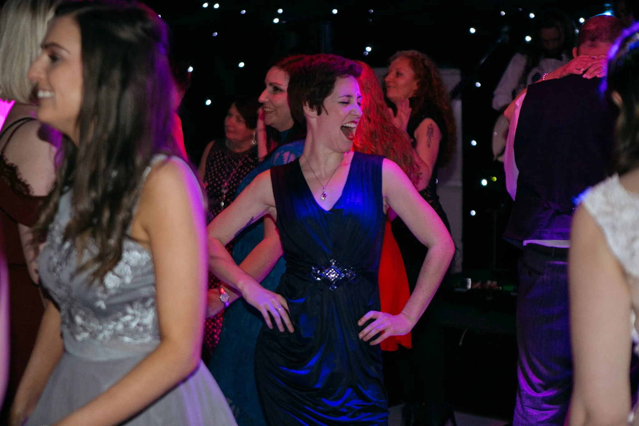Wedding guests laughing and dancing together under colourful lights