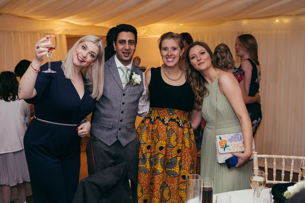 The groom and three wedding guests posing together beside the reception tables