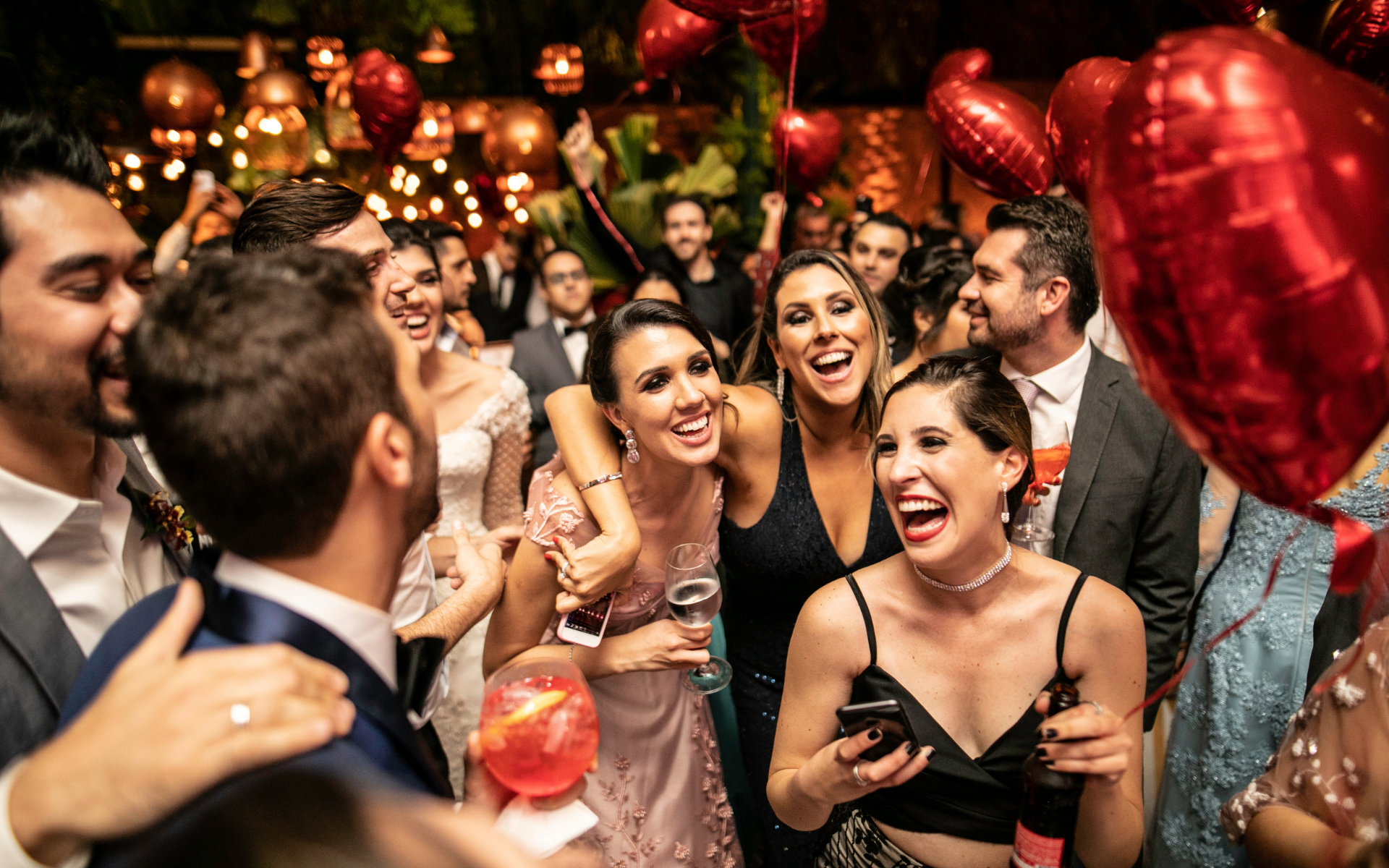 Wedding guests celebrating together beneath red heart-shaped balloons