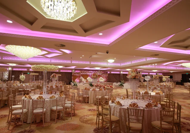 Wedding reception tables with gold chairs, chandeliers and pink ceiling lighting at Grand Sapphire
