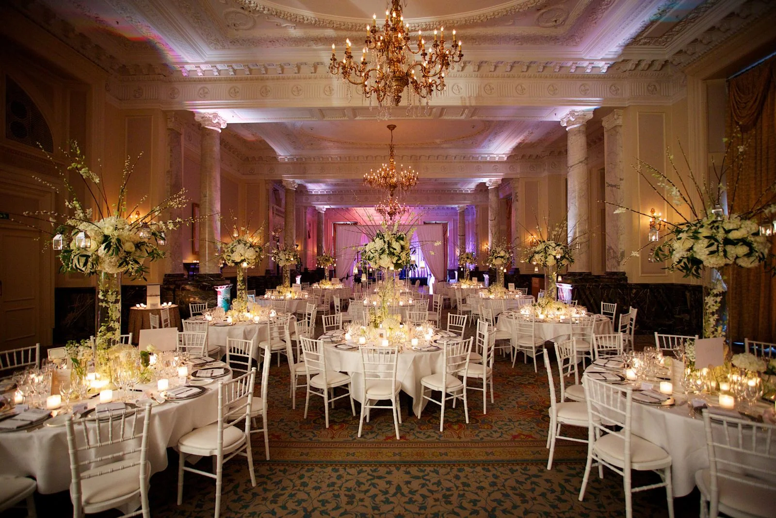 Candlelit wedding tables with tall white flower arrangements, marble columns and chandeliers at The Landmark London