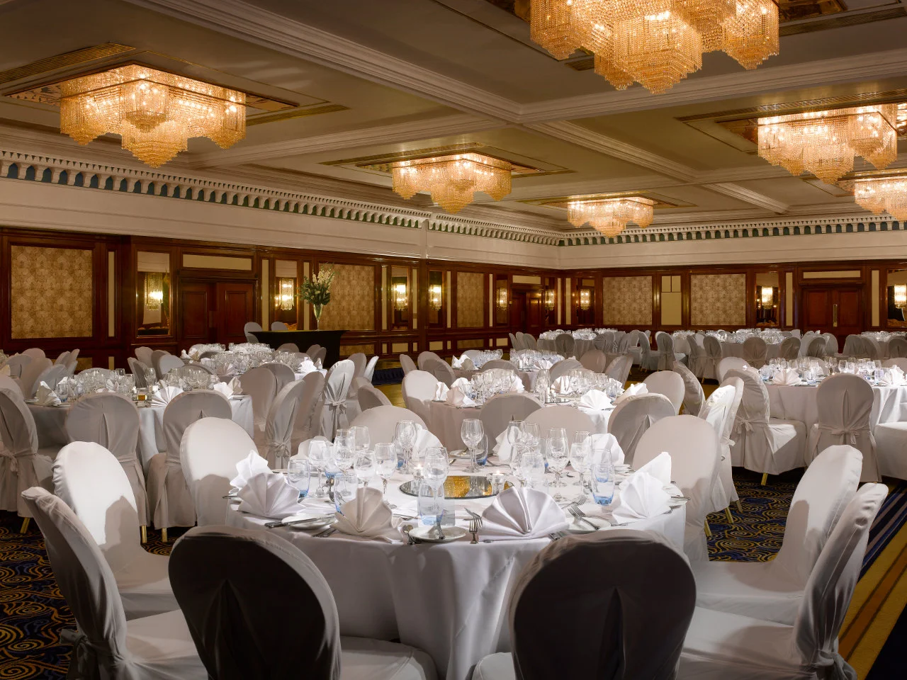 White-covered wedding tables and chairs beneath crystal chandeliers in the former Radisson Blu Portman Square ballroom