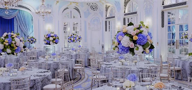 Wedding reception tables with clear chairs and pastel flower arrangements in a pale blue and white room at The Savoy
