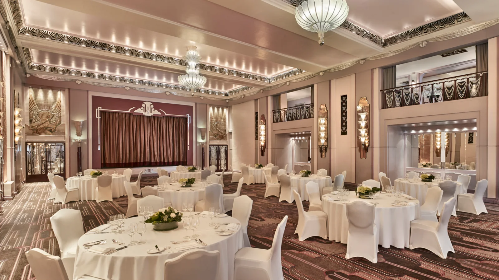 Round dining tables and white-covered chairs facing the curtained stage in the Sheraton Grand’s Art Deco ballroom