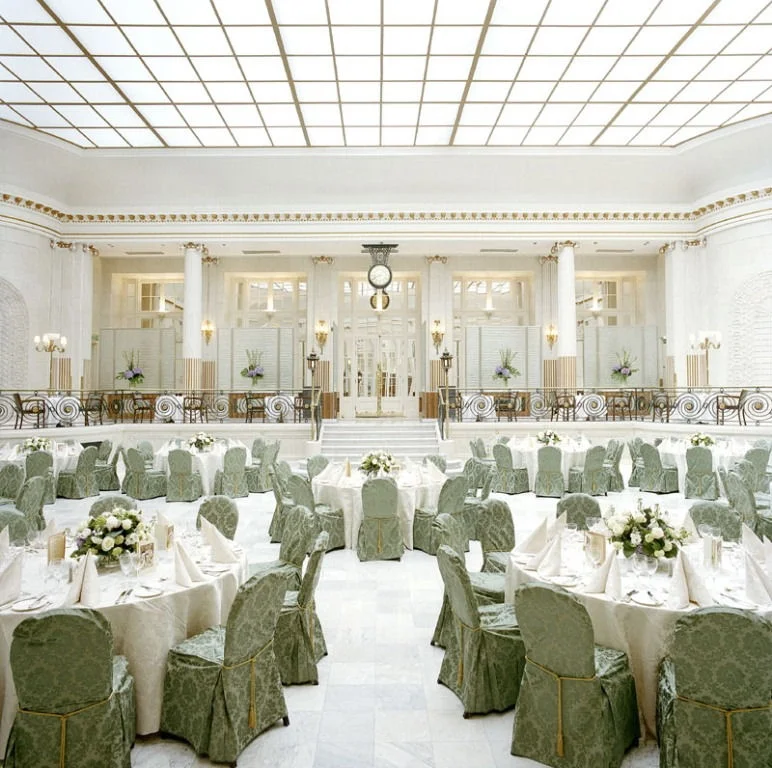 Wedding breakfast tables with green patterned chair covers beneath the Waldorf Hilton’s bright gridded glass ceiling